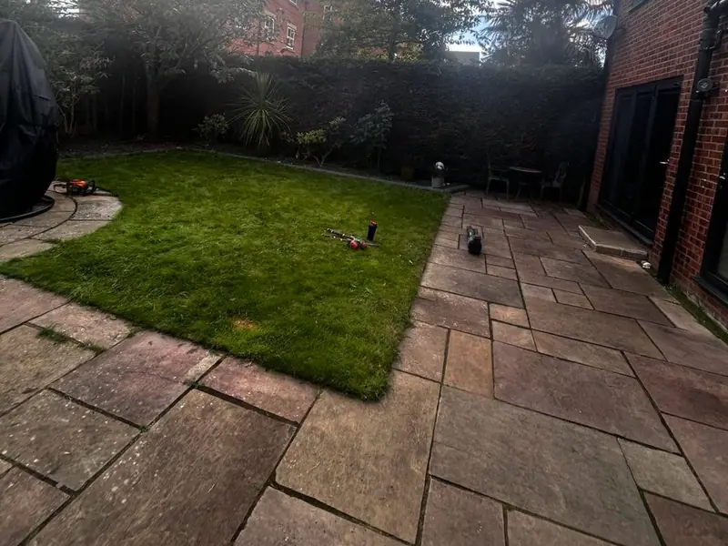 Sandstone patio running along the side of a lawn behind a brick house