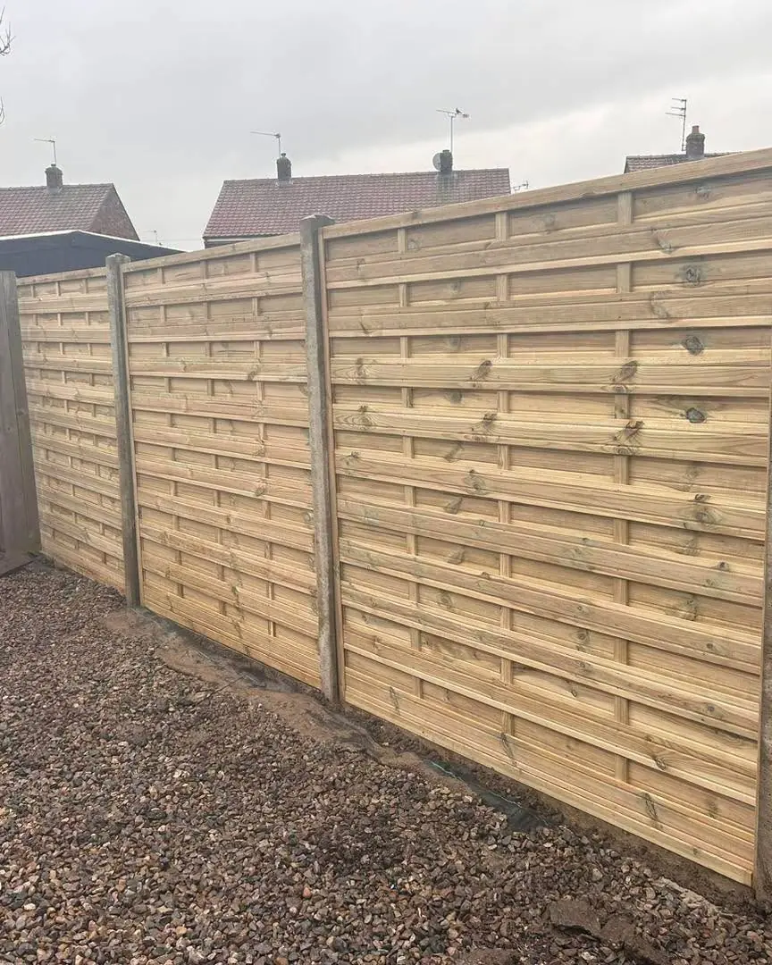 Horizontal slatted fence panels between concrete posts above a gravel strip
